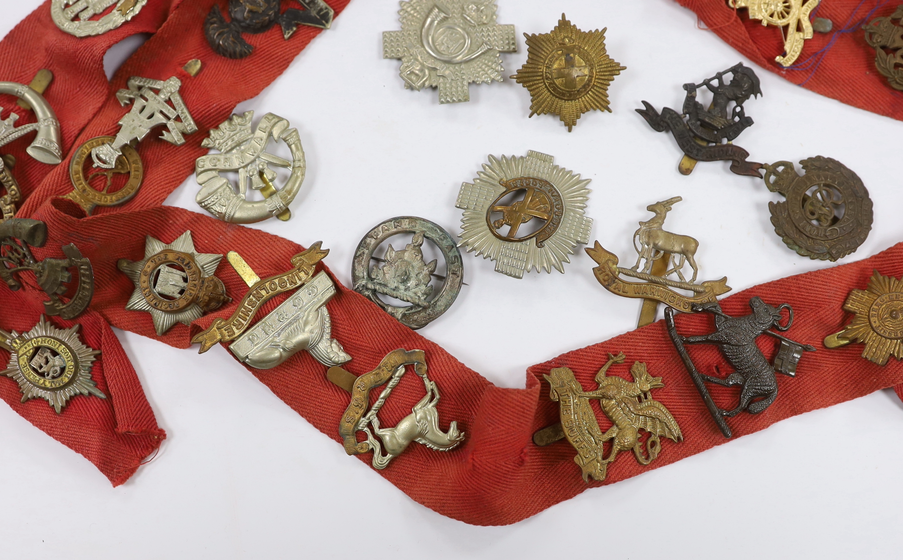Thirty-two military cap badges, including; The Devonshire Reg., The Buffs, RFC, Royal Artillery, The Royal Sussex Reg. Royal Warwickshire Reg., Cornwall, etc.